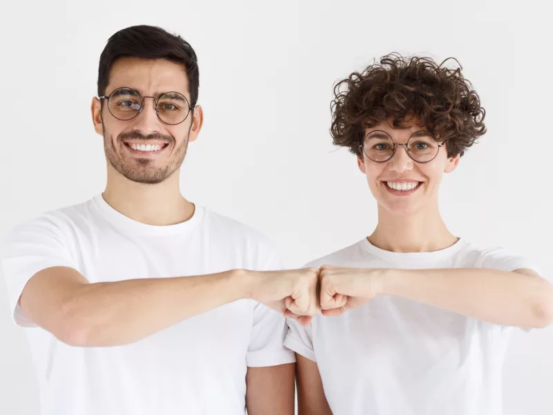 Foto eines Mannes und einer Frau mit einer Brille und einer Kurzhaarfrisur, die sich die Faust geben